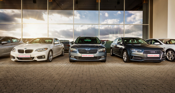 Diverse Autos stehen vor einem Glasgebäude der Deutsche Leasing